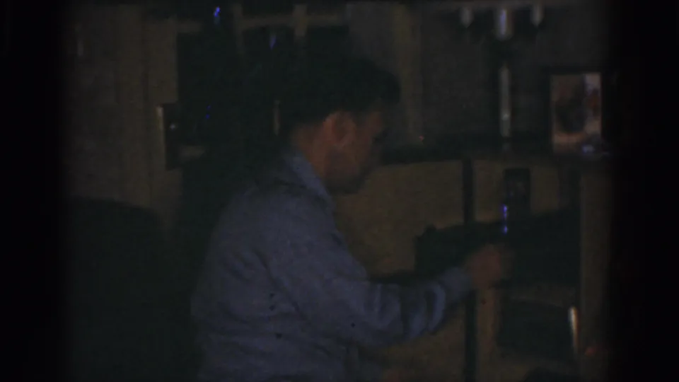 The man, seen in profile, reaches toward a small control or object on a dark surface in the Omaha interior.