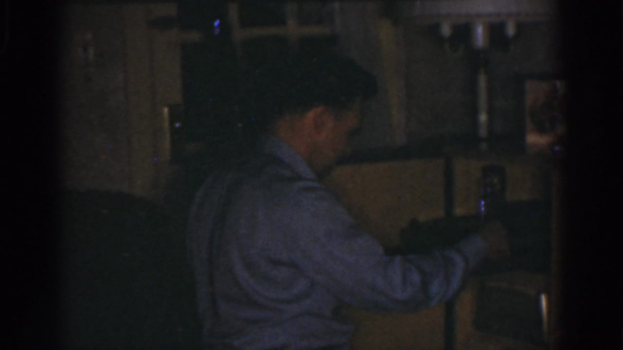 Man stands side-on while placing or holding an object near a shelf.