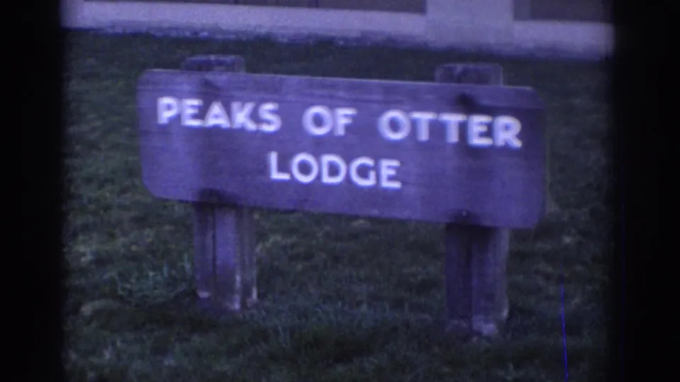 1971 8mm frame showing a wooden Peaks of Otter Lodge sign in Bedford, Virginia, bordered by visible film gate edges.