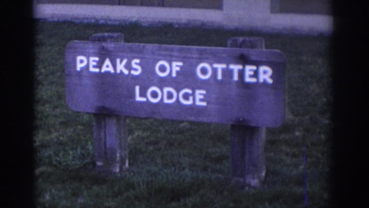 The Peaks of Otter Lodge sign remains centered in a soft 8mm exterior view, with grass and part of a structure behind it.