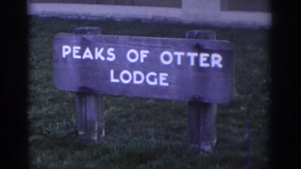 The Peaks of Otter Lodge sign remains centered in a soft 8mm exterior view, with grass and part of a structure behind it.