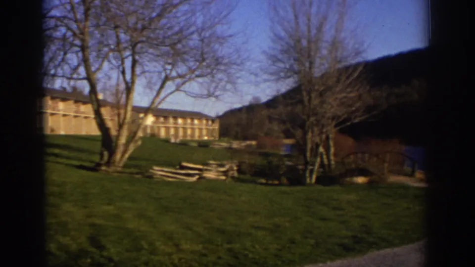 1971 Bedford, Virginia 8mm frame showing a low balcony building beyond a green lawn, bare trees, and a wooded hillside.