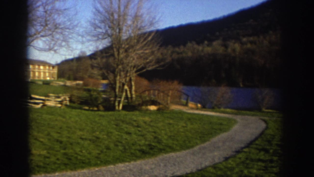 1971 Bedford, Virginia 8mm frame with a winding gravel path through lawn, bare trees, blue retaining wall, and small distant figures.
