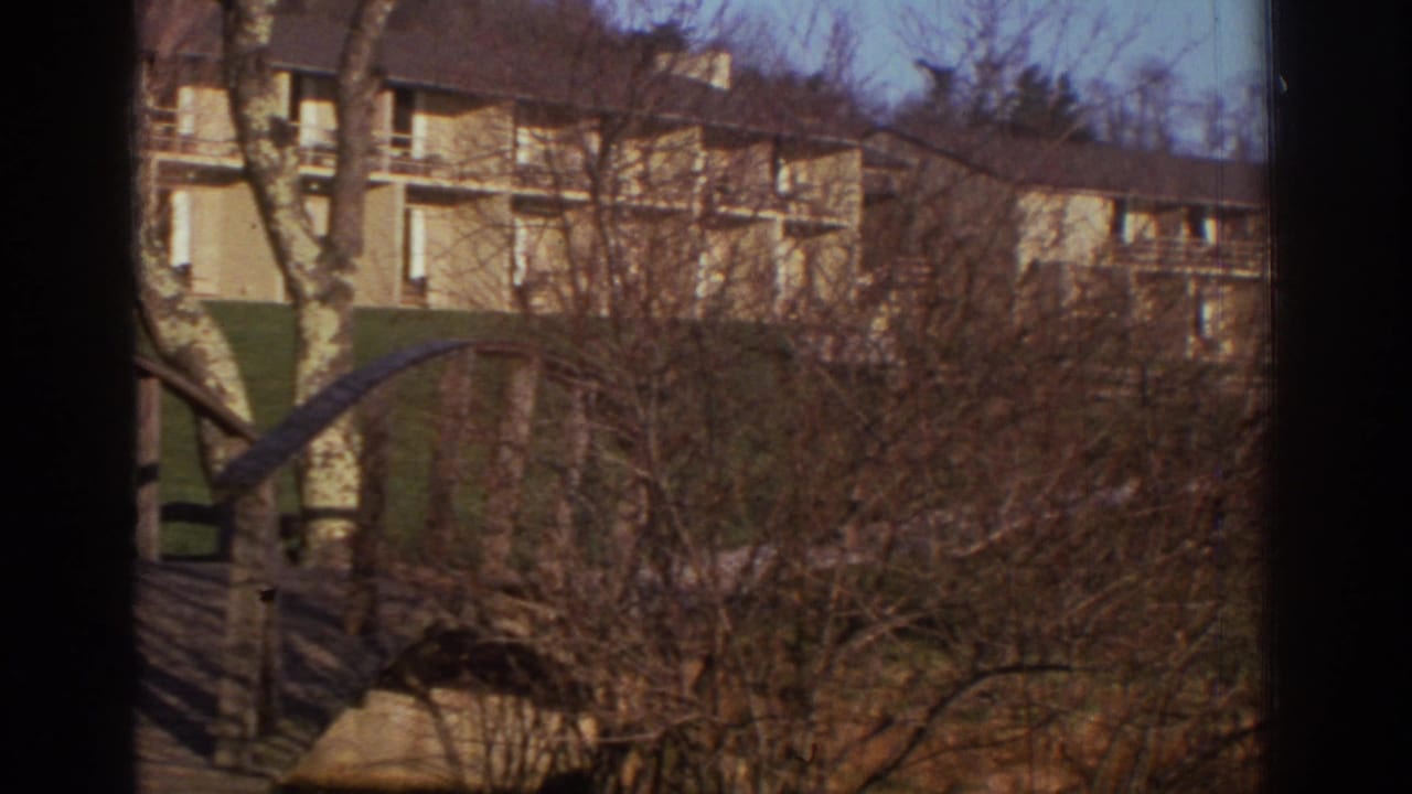 The pan continues across Bedford apartment buildings, with bare trees and part of the wooden bridge obscuring the view.
