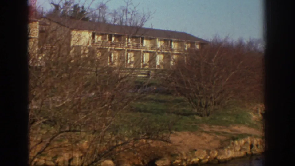 1971 Bedford, Virginia home-movie frame showing a large lodge-like building beyond bare trees in a wooded mountain setting.