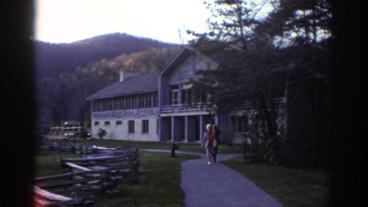 Older couple walks along a paved path near a lodge-style building in Bedford, Virginia, with wooded hills in the background.