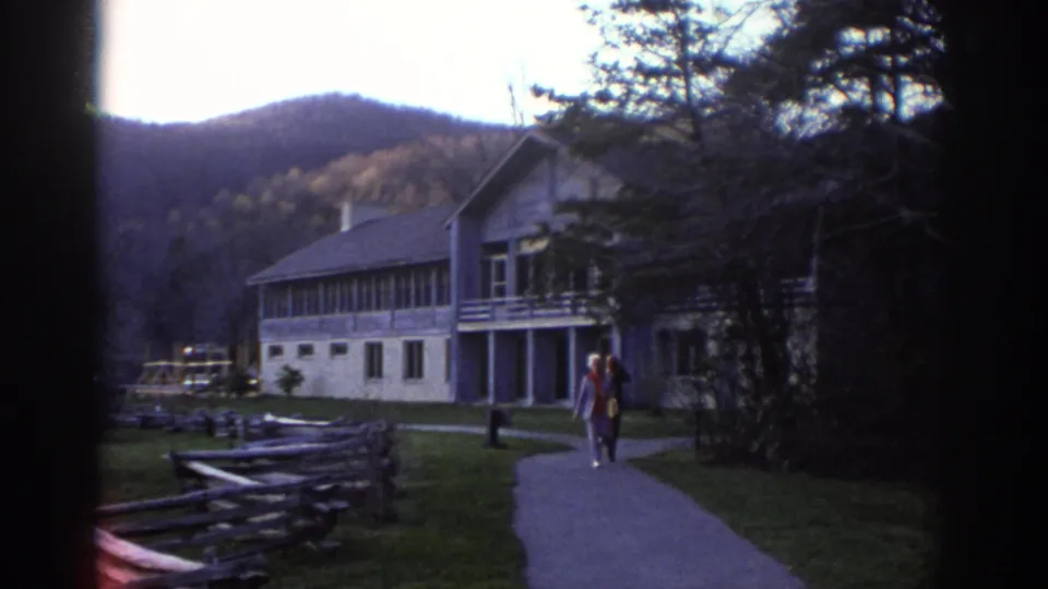 Older couple walks along a paved path near a lodge-style building in Bedford, Virginia, with wooded hills in the background.