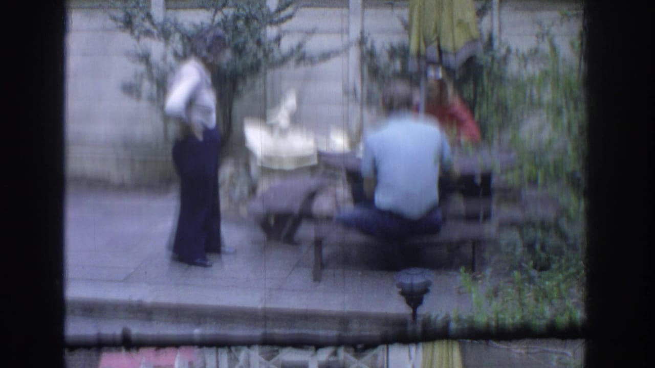 Adults gather on a backyard patio near a wooden picnic table and garden fountain.