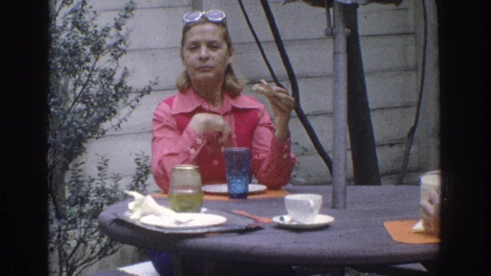 1971 Miami frame of a woman with sunglasses on her head seated at an outdoor lunch table.
