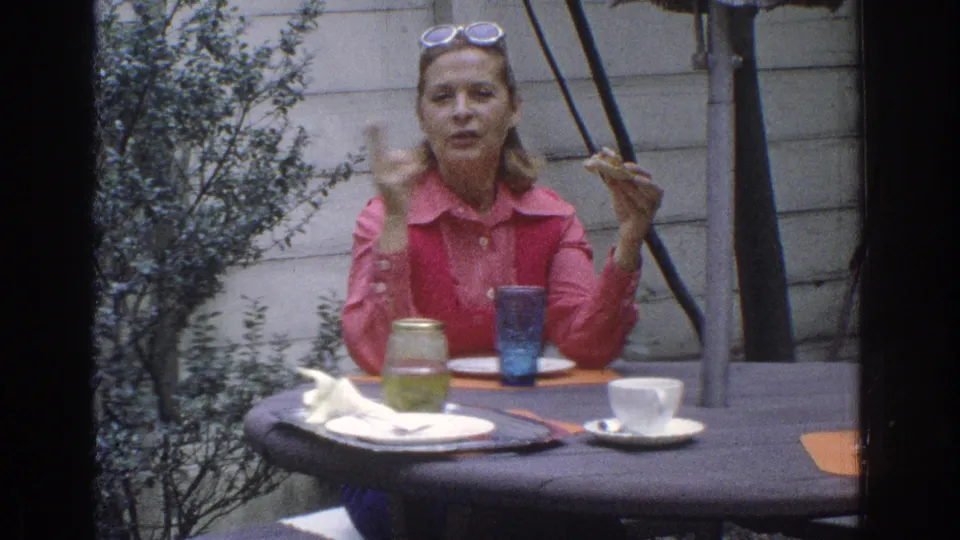 1971 Miami home-movie frame showing a woman gesturing during conversation at an outdoor lunch table.