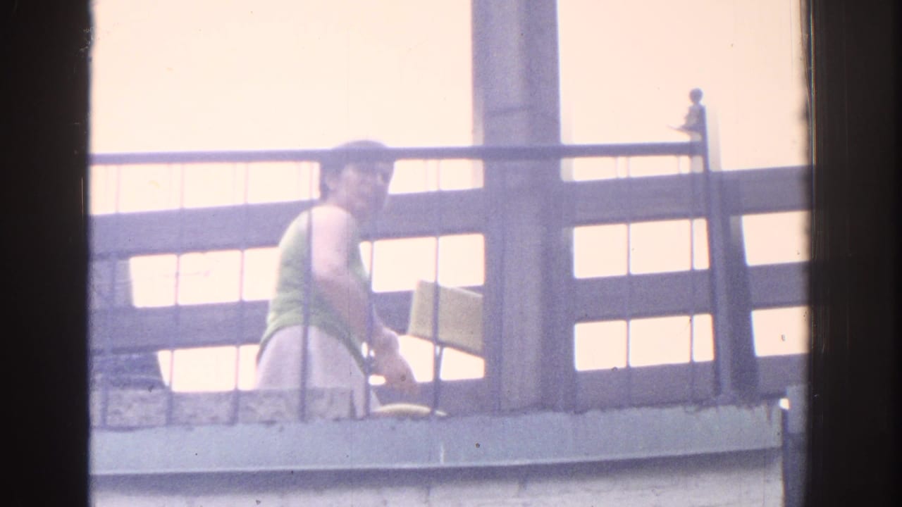 Woman in a green sleeveless top seated on a balcony behind railings.