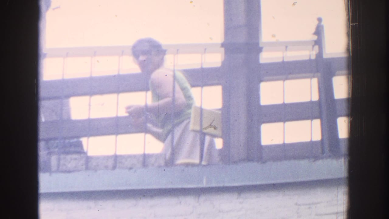 Woman in a green top seated or crouched near a balcony railing in bright light.