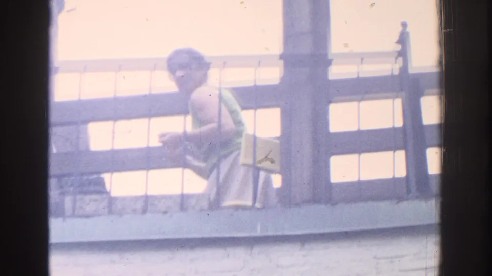 1971 Miami home-movie frame showing a woman in a green top near a balcony railing, partly softened by exposure and film haze.