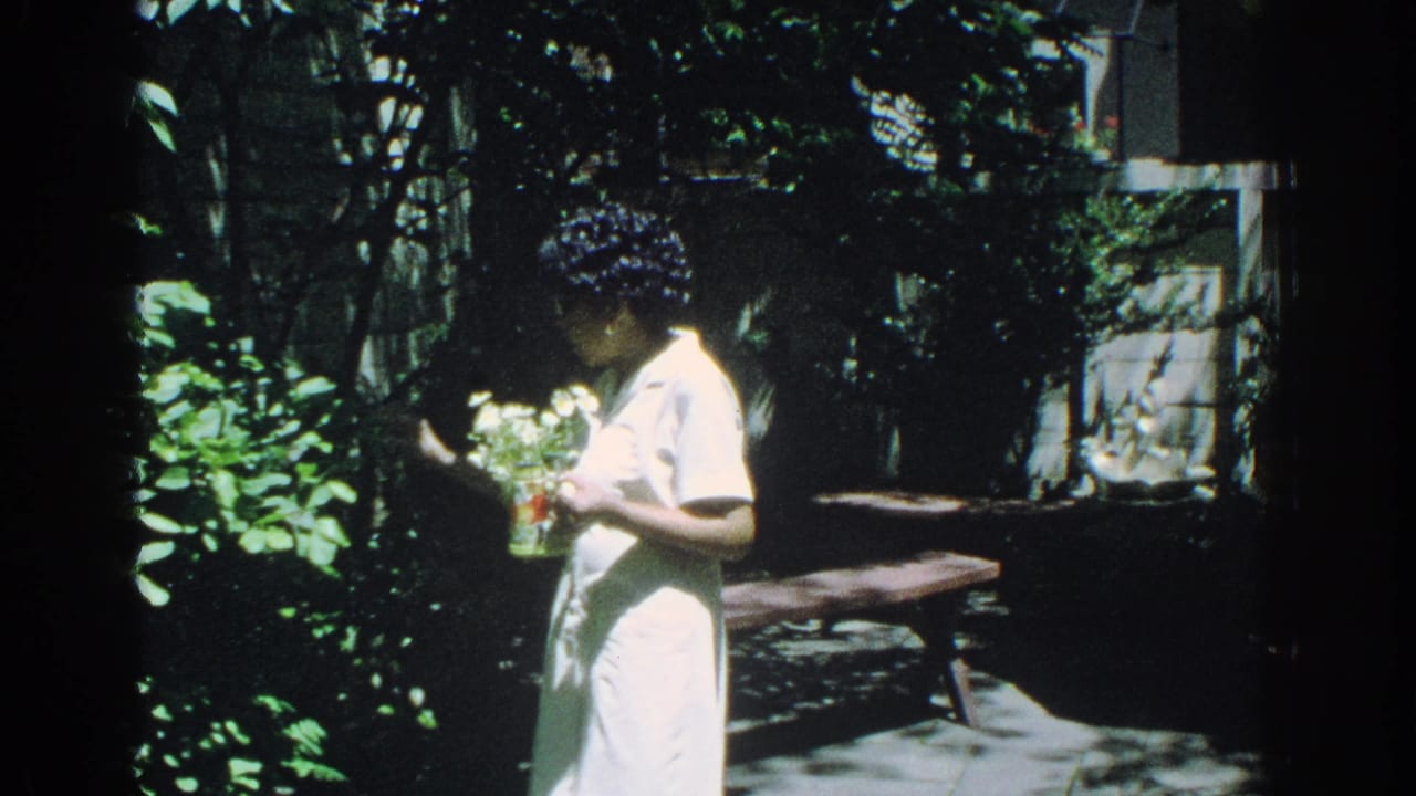 Woman in a white dress standing in a shaded garden while holding flowers.
