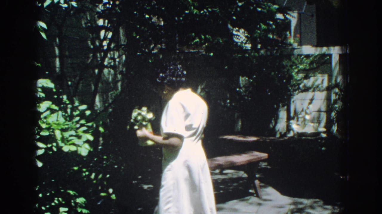 Woman in profile holding a small bouquet beside leafy plants and a patio bench.