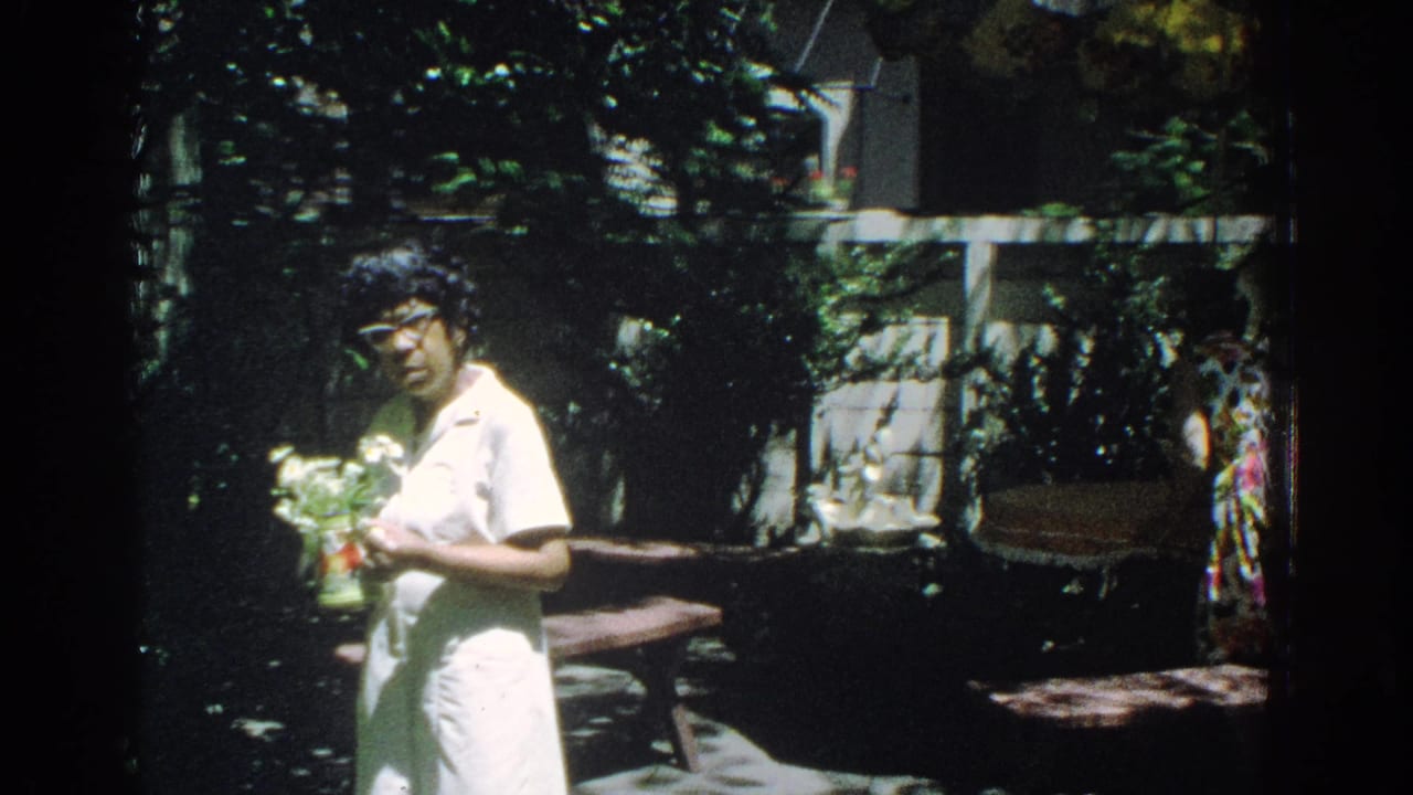 Woman in a white dress holding flowers in a shaded backyard.