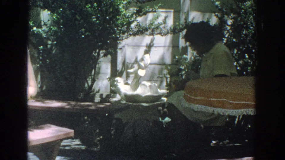 1971 Miami 8mm frame with a partially silhouetted person by a round table, white fence, plants, and shaded patio details.