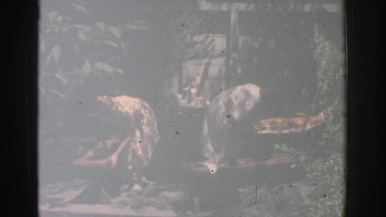 Two women bend over outdoor decorative objects in a shaded garden.