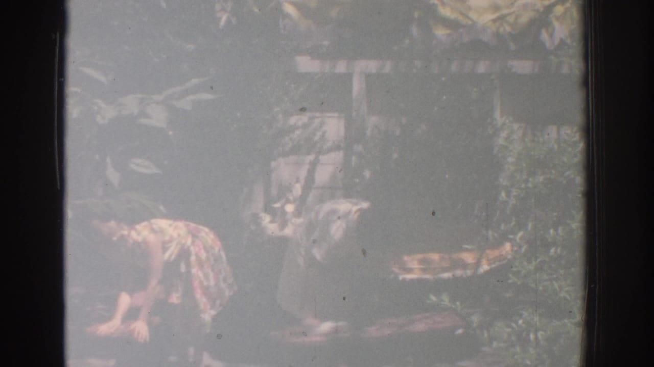Two women continue cleaning outdoor objects beside plants and patio decor.
