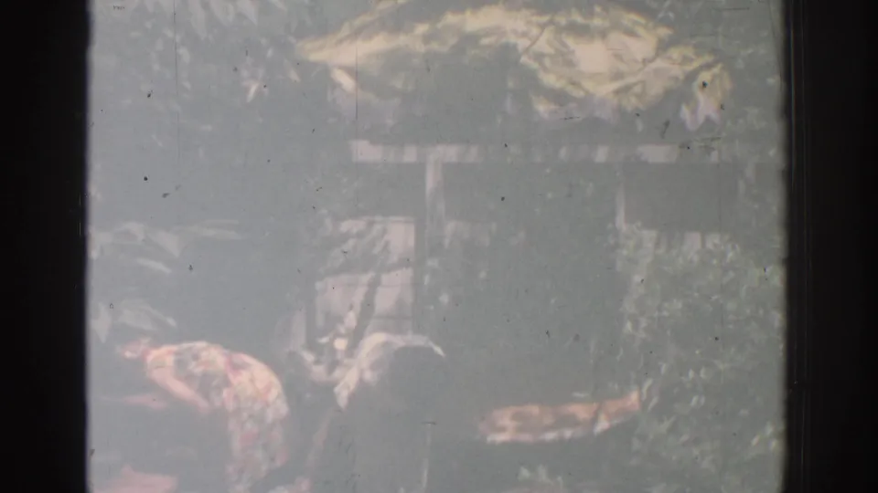 Faded 8mm frame from 1971 Miami showing women working among patio decorations and greenery in bright outdoor light.