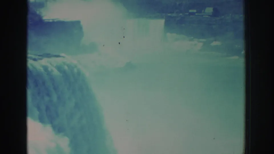 1971 home-movie frame showing a cropped close view of Niagara Falls water rolling over the brink into heavy mist and aged-film specks.