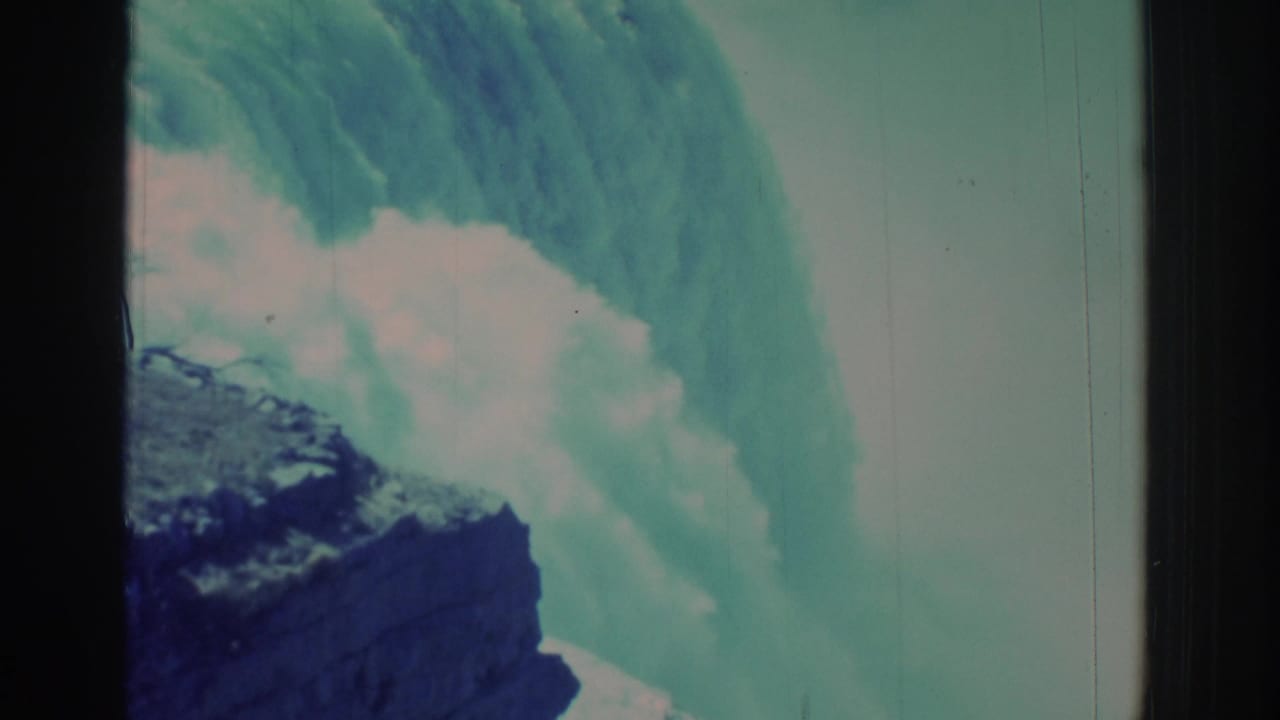 Waterfall and mist seen beside a dark vertical film frame bar and rocky cliff.