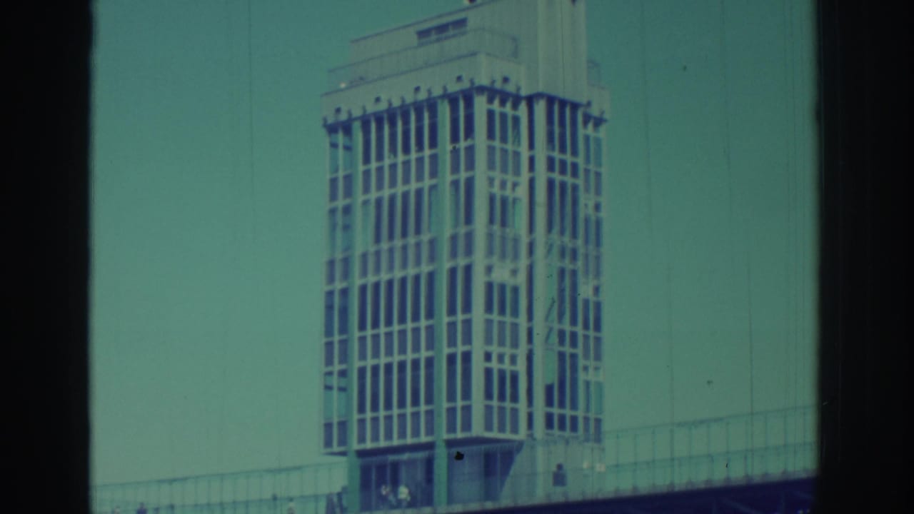 1971 Niagara Falls frame with the tower, bridge railings, small pedestrians, and a teal color cast from aged 8mm film.