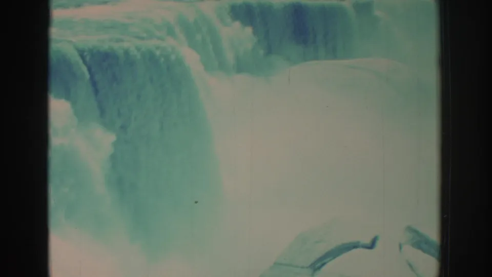 1971 Niagara Falls home-movie frame focused on rushing water and mist, with a curved foreground railing and aged 8mm color shift.