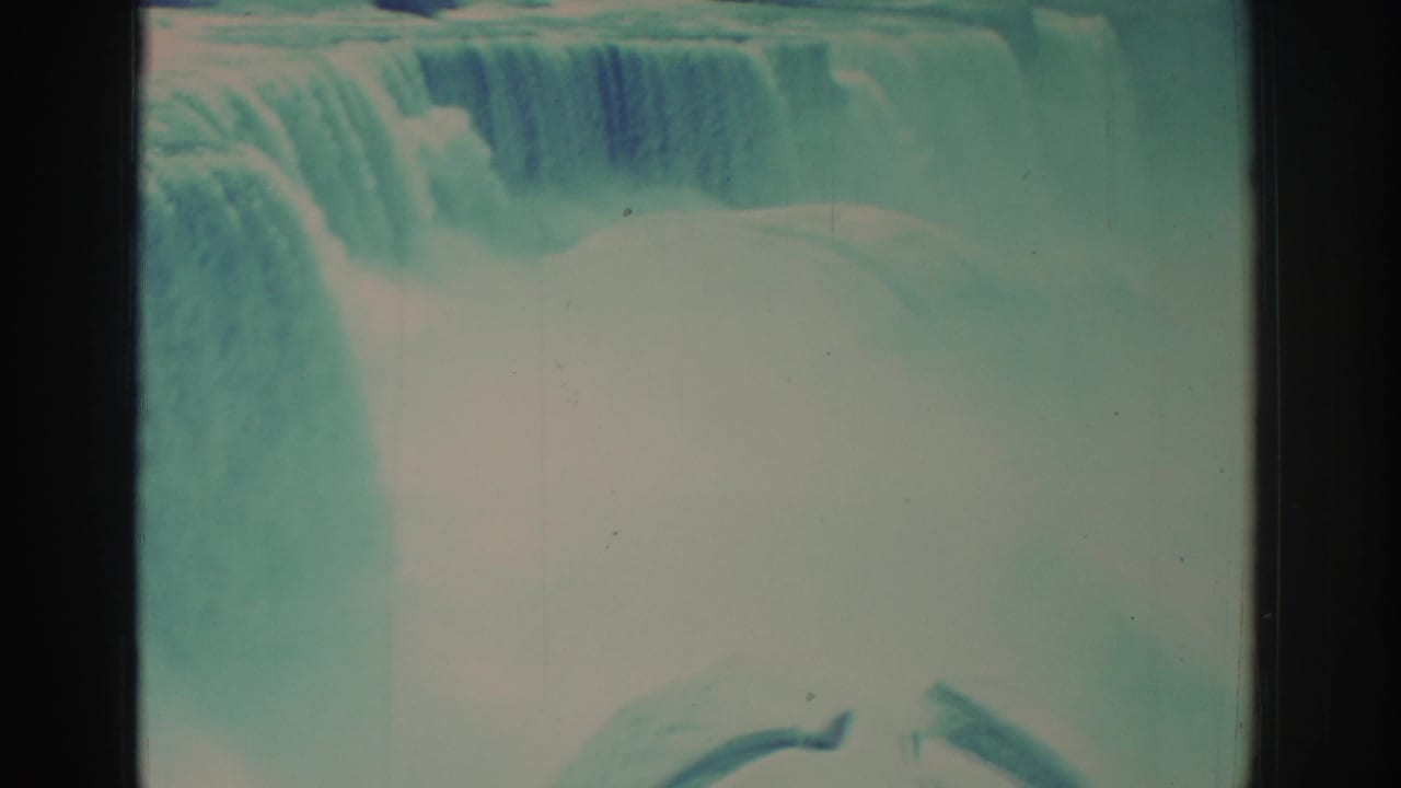 1971 8mm home-movie frame of Niagara Falls showing the upper cascade, dense mist, and aged teal-blue film color.
