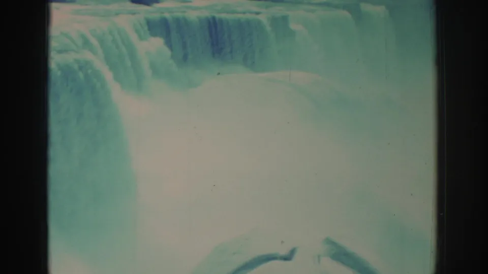 1971 8mm home-movie frame of Niagara Falls showing the upper cascade, dense mist, and aged teal-blue film color.