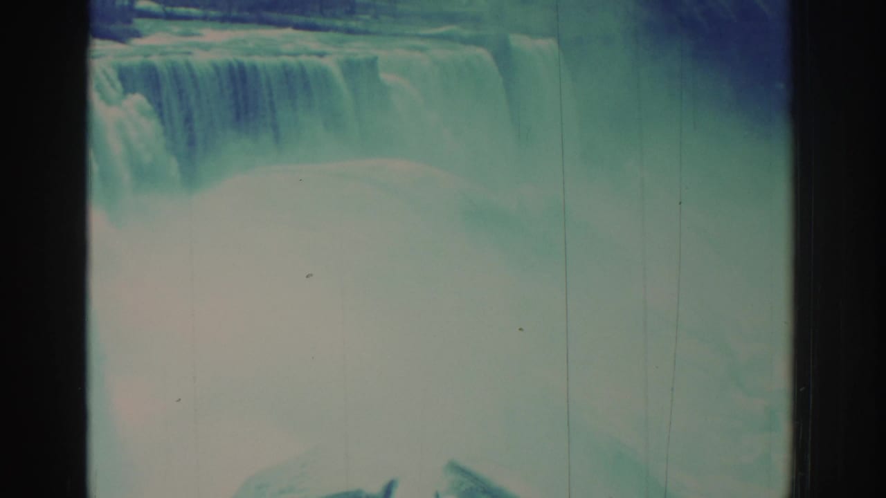 Waterfall crest and pale mist framed by faded color film and vertical scratches.