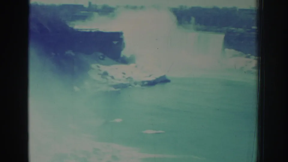 1971 Niagara Falls home-movie frame with bright mist, river surface, distant shoreline, and aged 8mm film texture.