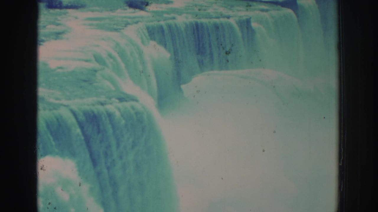 Wide waterfall curtains dropping into mist with teal-blue color and film scratches.