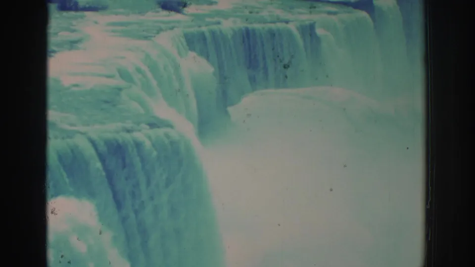 1971 8mm view of Niagara Falls, showing broad cascading water, rising mist, teal-blue fading, and dark frame edges.