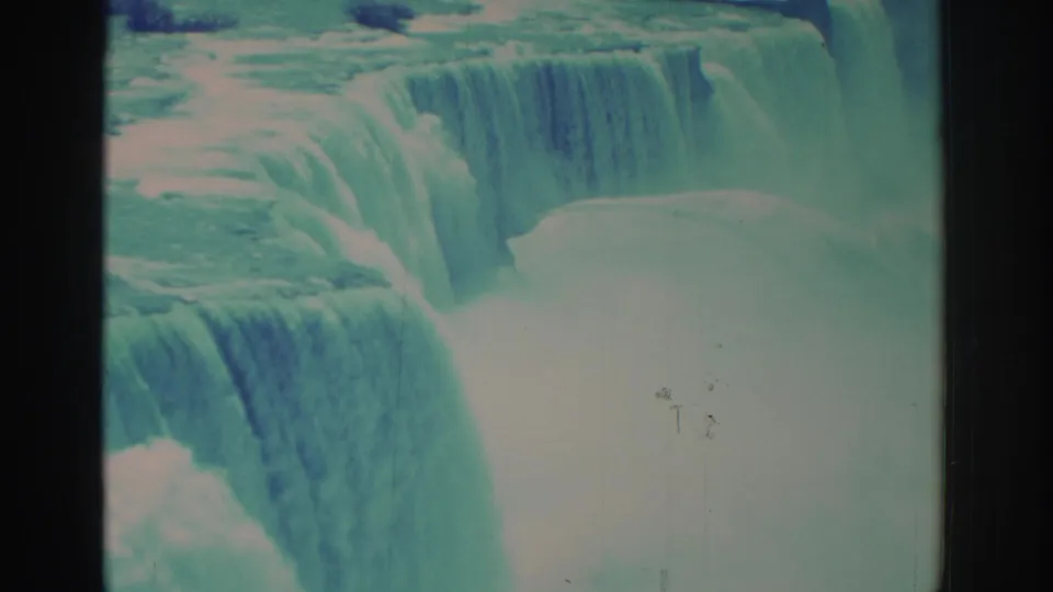Closer 1971 8mm Niagara Falls frame with layered cascades, foaming water, mist at the base, and small surface scratches.
