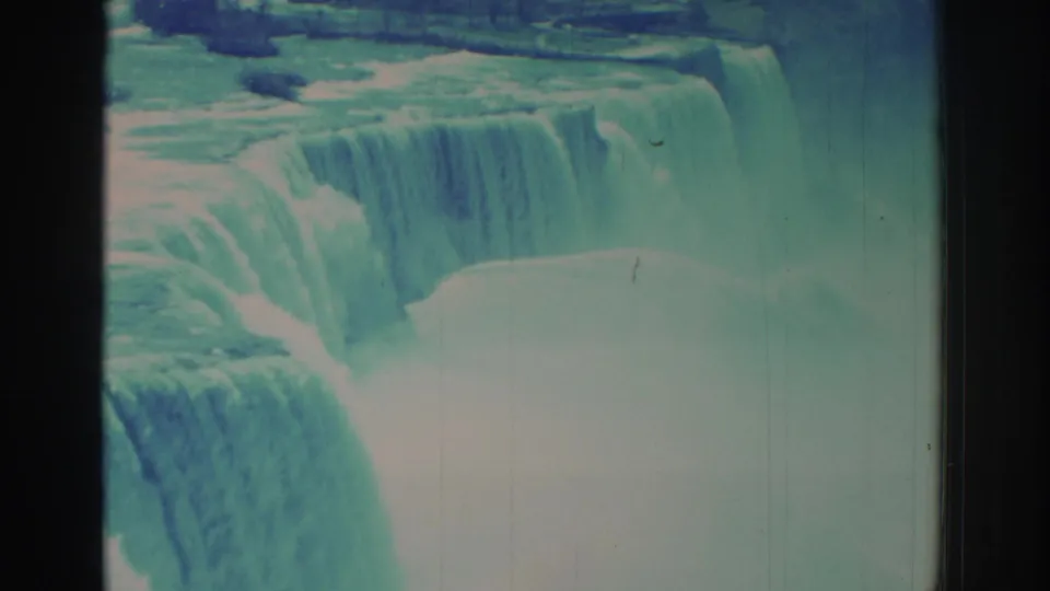 1971 8mm Niagara Falls frame showing a broad cascade, mist-filled basin, faded teal color, and rounded film-frame edges.