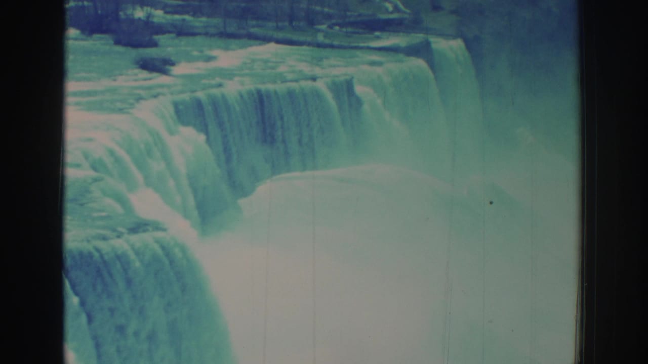 1971 8mm-style home-movie frame of Niagara Falls, showing a broad cascade, bright mist, and dark film edges.