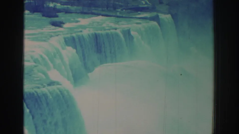 1971 8mm-style home-movie frame of Niagara Falls, showing a broad cascade, bright mist, and dark film edges.