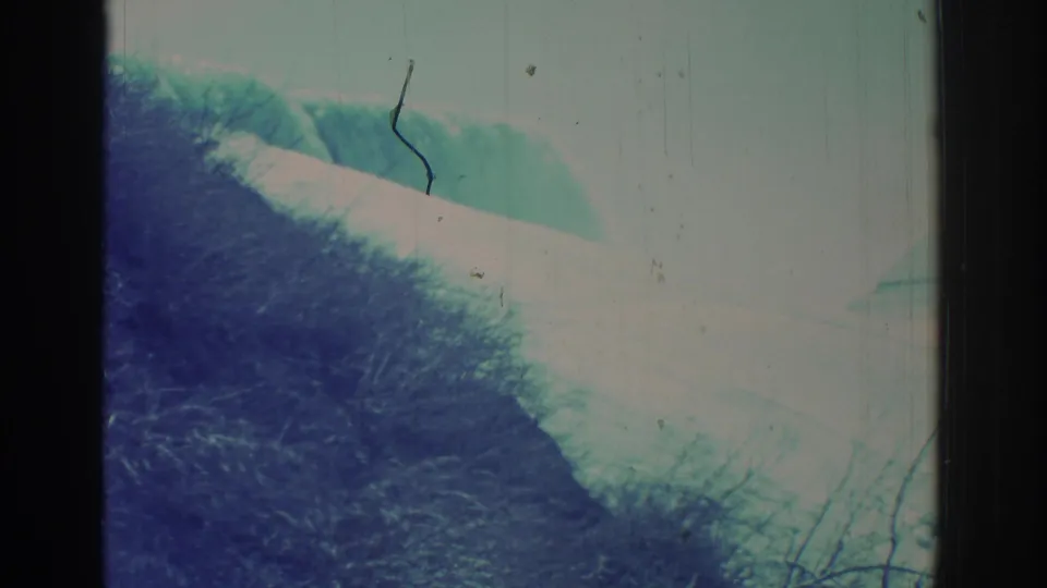 Archival 8mm frame of Niagara Falls from a shoreline vantage, showing water dropping away, brush, and overexposed mist.