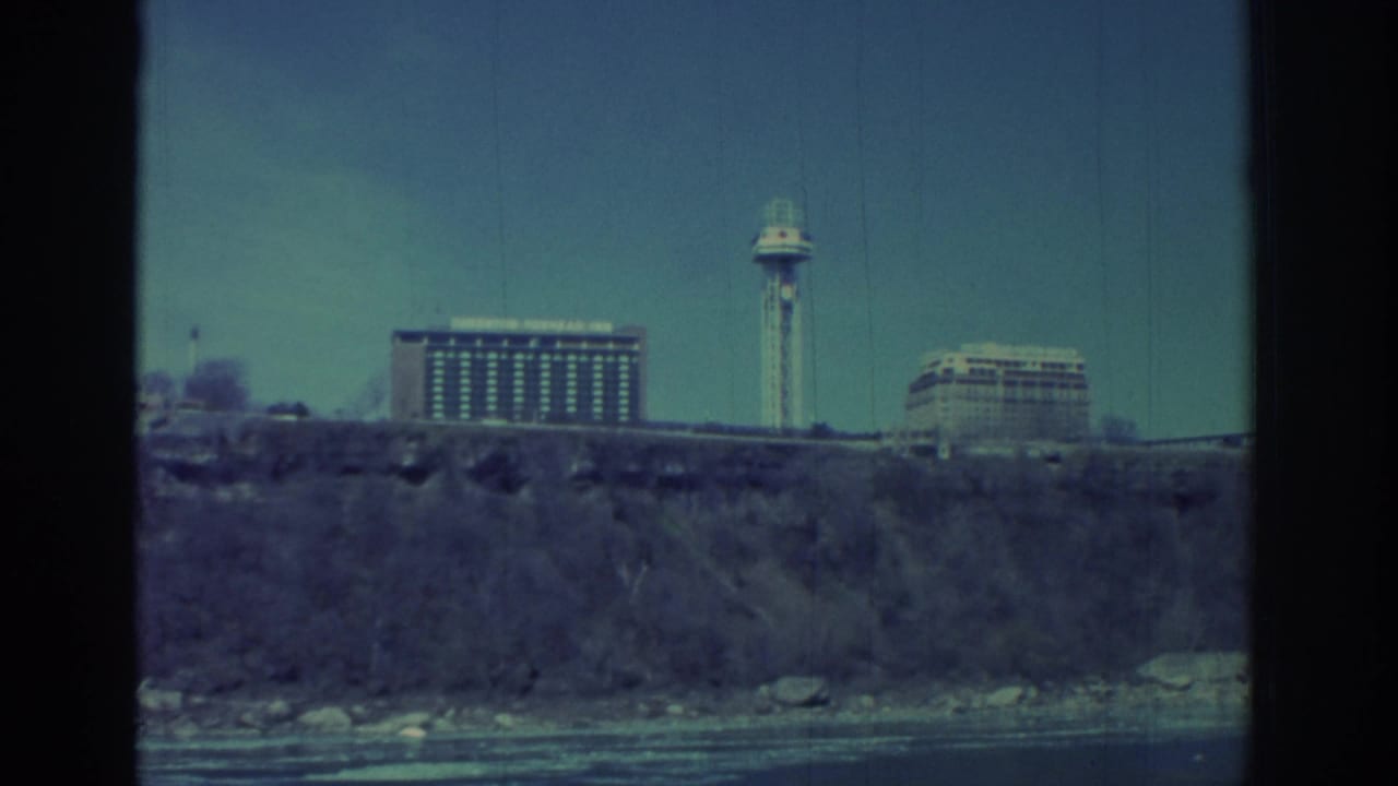 1971 Niagara Falls-area home-movie frame showing large cliffside buildings and an observation tower across the water.