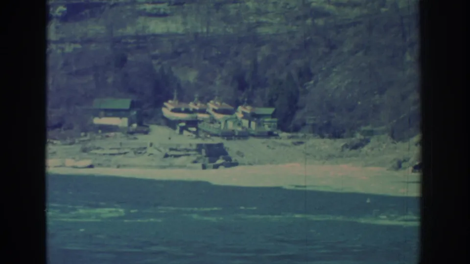 1971 Niagara Falls-area frame showing a distant waterfront cluster with boats and buildings below a wooded slope.