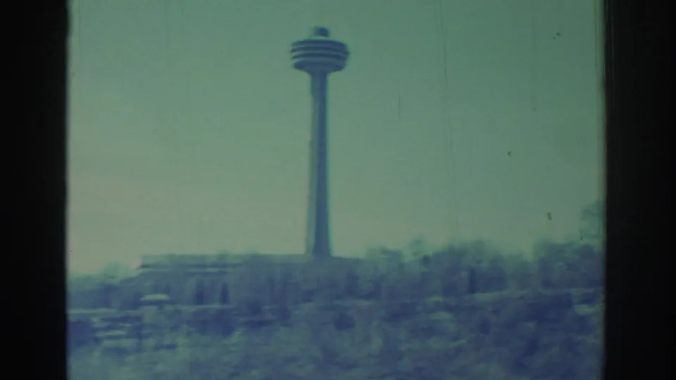 1971 8mm view of a distant observation tower near Niagara Falls, seen over snowy ground, bare trees, and a pale sky.