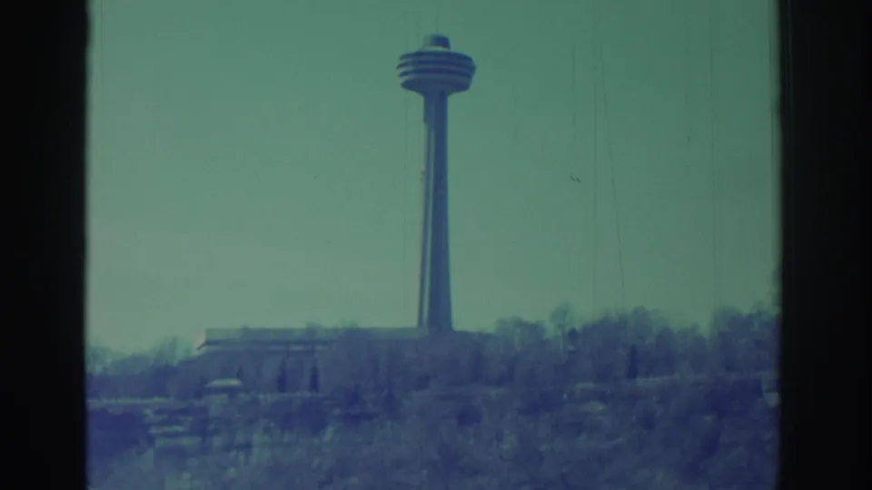 Faded 8mm frame showing the distant Skylon Tower area above bare winter trees and snow near Niagara Falls.