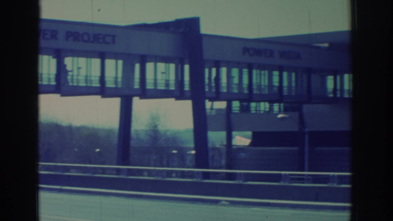1971 Niagara Falls-area 8mm frame showing a POWER VISTA building and enclosed elevated walkway beyond highway guardrails.