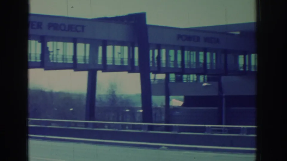 1971 Niagara Falls-area 8mm frame showing a POWER VISTA building and enclosed elevated walkway beyond highway guardrails.
