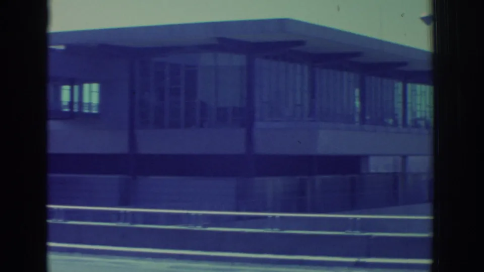 1971 Niagara Falls-area 8mm view of the modernist building's lower glass facade and broad flat canopy near a road.