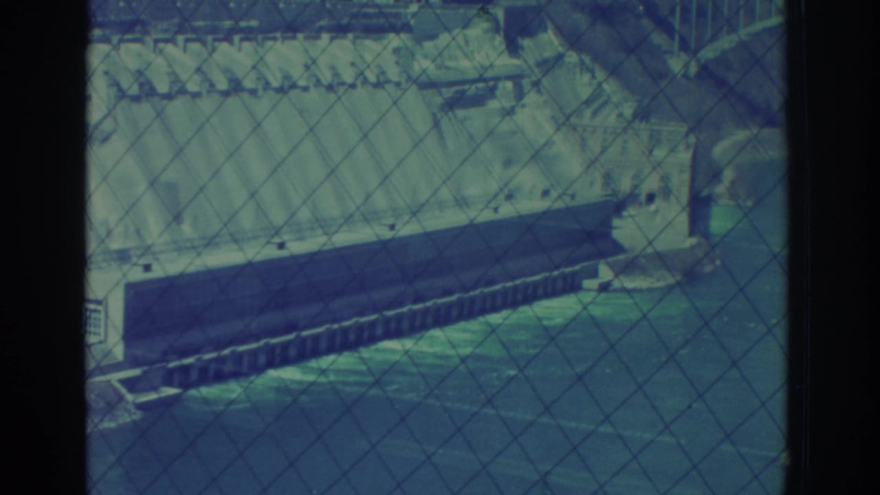 1971 Niagara Falls, New York 8mm frame showing a dam or power station structure across water, viewed through safety fencing.
