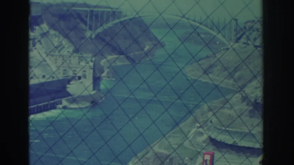 Niagara Falls hydroelectric dam area and river channel seen through safety fencing in aged blue-green 8mm footage from 1971.