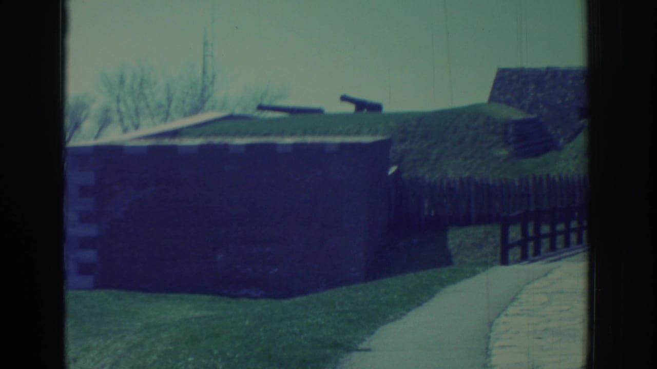 1971 8mm view of a historic fort near Niagara Falls, with dark walls, grassy earthworks, cannons, and a curved path.