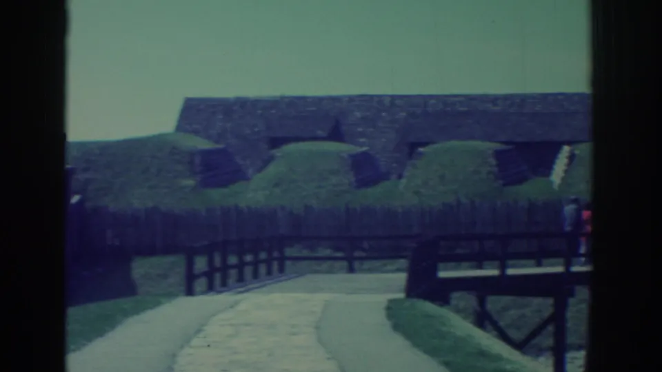 1971 home-movie frame of fort ramparts, cannons, a wooden bridge, and a pale walkway at a historic site near Niagara Falls.